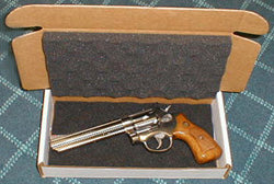 A pistol in a cardboard box on a checkered fabric background