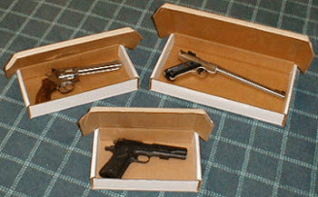 Three guns in cardboard boxes on a checkered surface